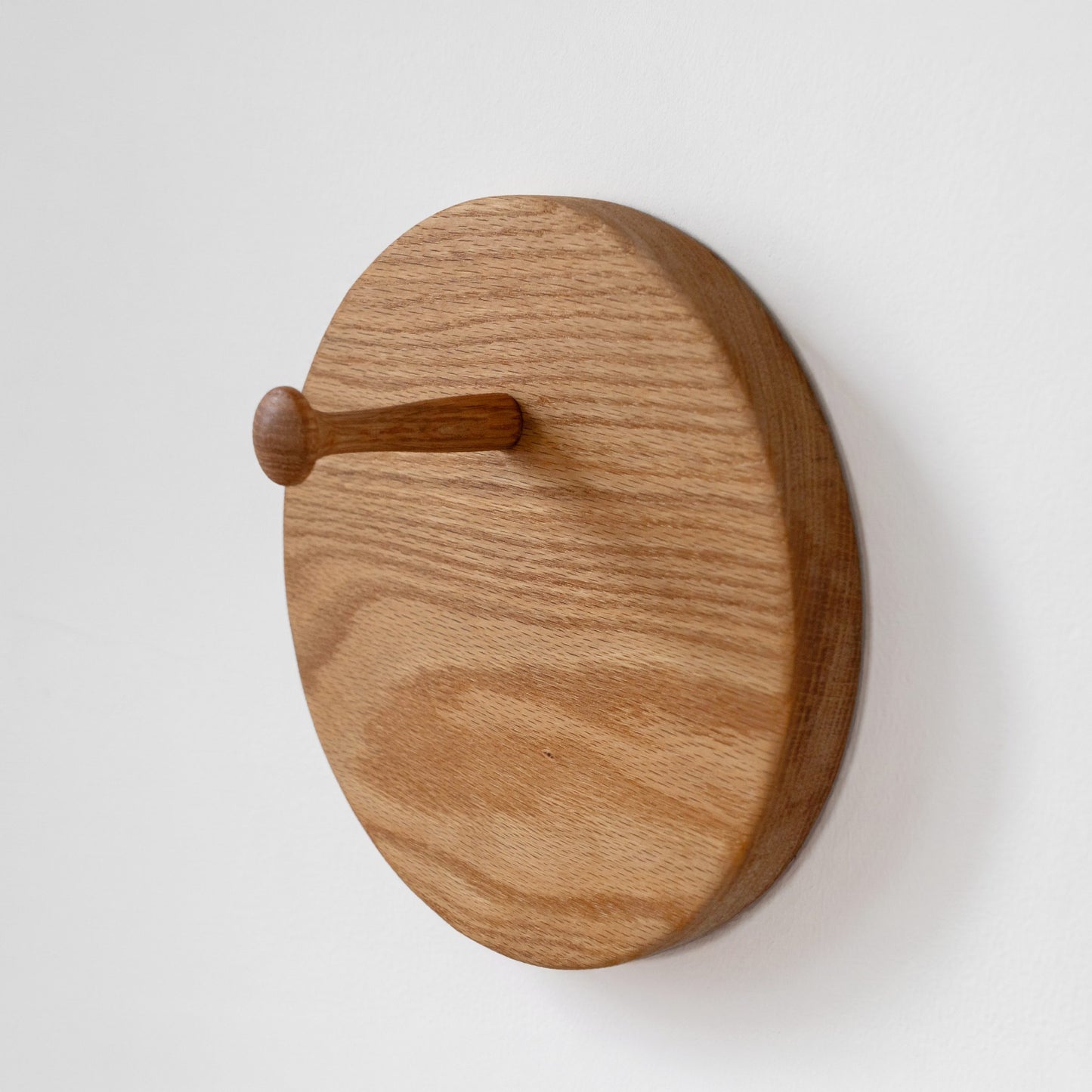A round wooden wall hook with a natural oak finish and visible wood grain, mounted on a plain white wall.