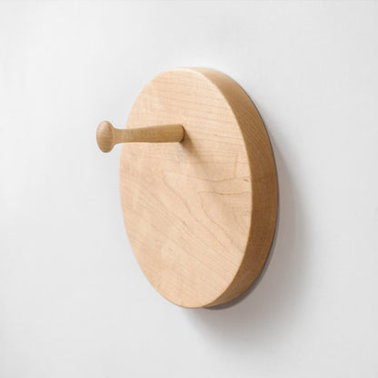 A minimalist round wooden peg hook mounted on a plain white wall, featuring a natural light wood finish and visible grain.