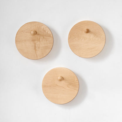 Three round light natural wood wall hooks with small wooden pegs, arranged on a clean white background.
