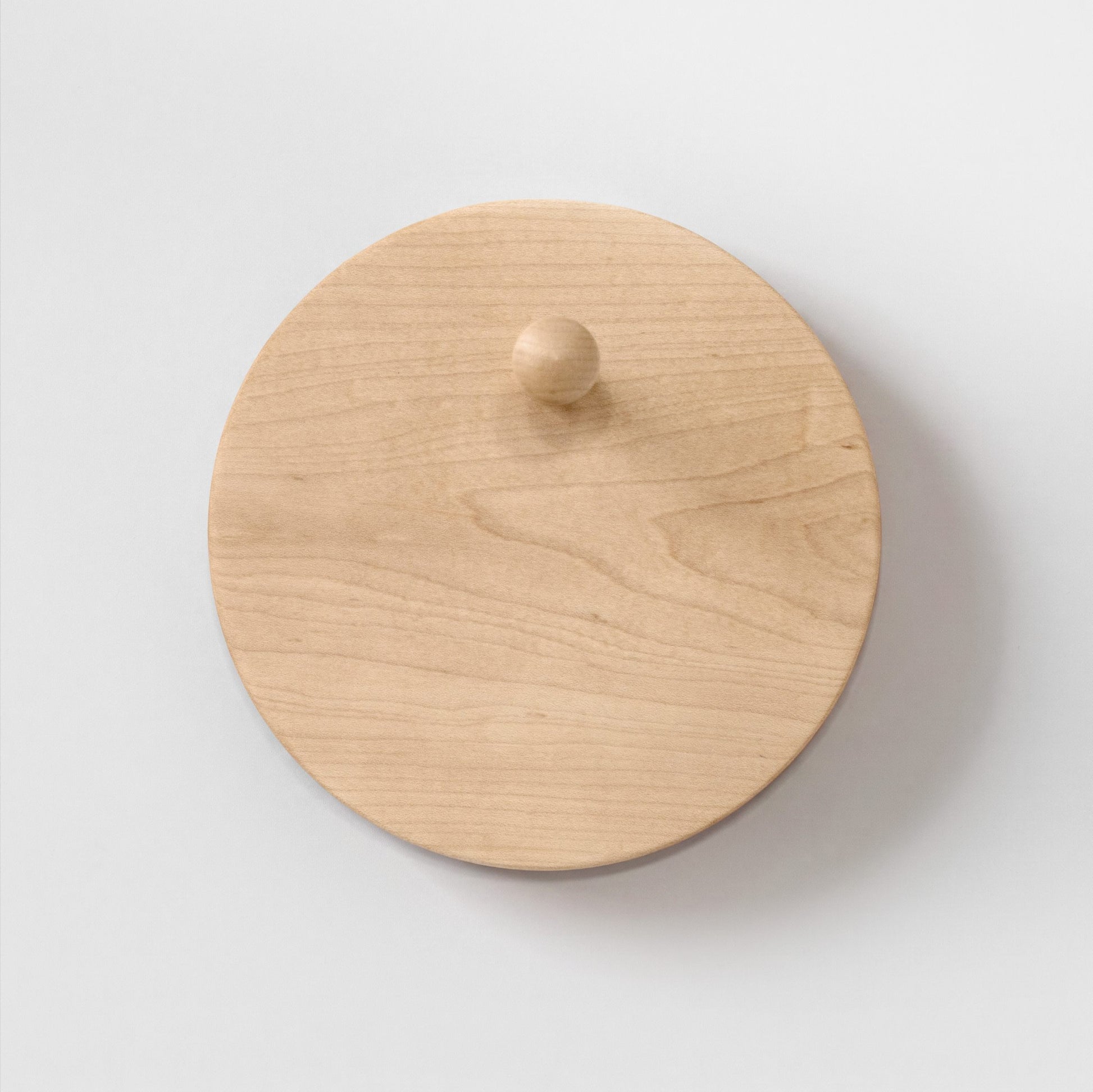 A round light maple wood hat rack with a small matching wooden peg, photographed from the front on a plain light background.