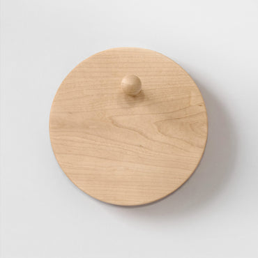 A round light maple wood hat rack with a small matching wooden peg, photographed from the front on a plain light background.