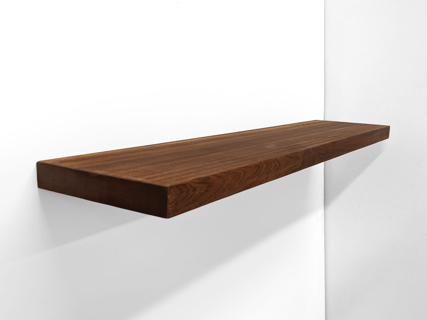 An extra-long, heavy-duty mahogany floating shelf is sucessfully installed and sits securely on a wall. Two hands grip the top and bottom of the front-facing side.