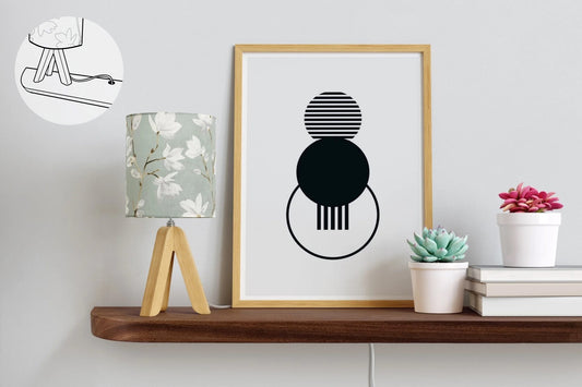 A mahogany floating shelf with rounded corners and a grommet hole is attached to a white wall with a lamp, picture, 3 books, and two plants on top as decor.