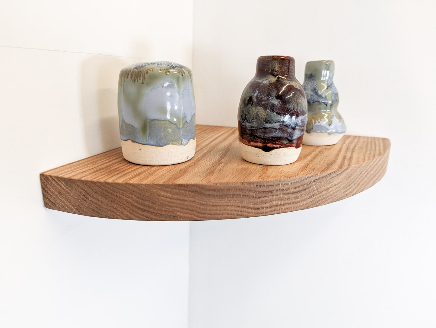 Three vases are displayed on top of an oak corner floating shelf with a rounded front face.