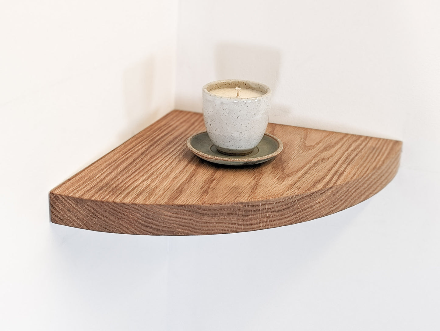 A candle is displayed on top of an oak corner floating shelf with a rounded front face.