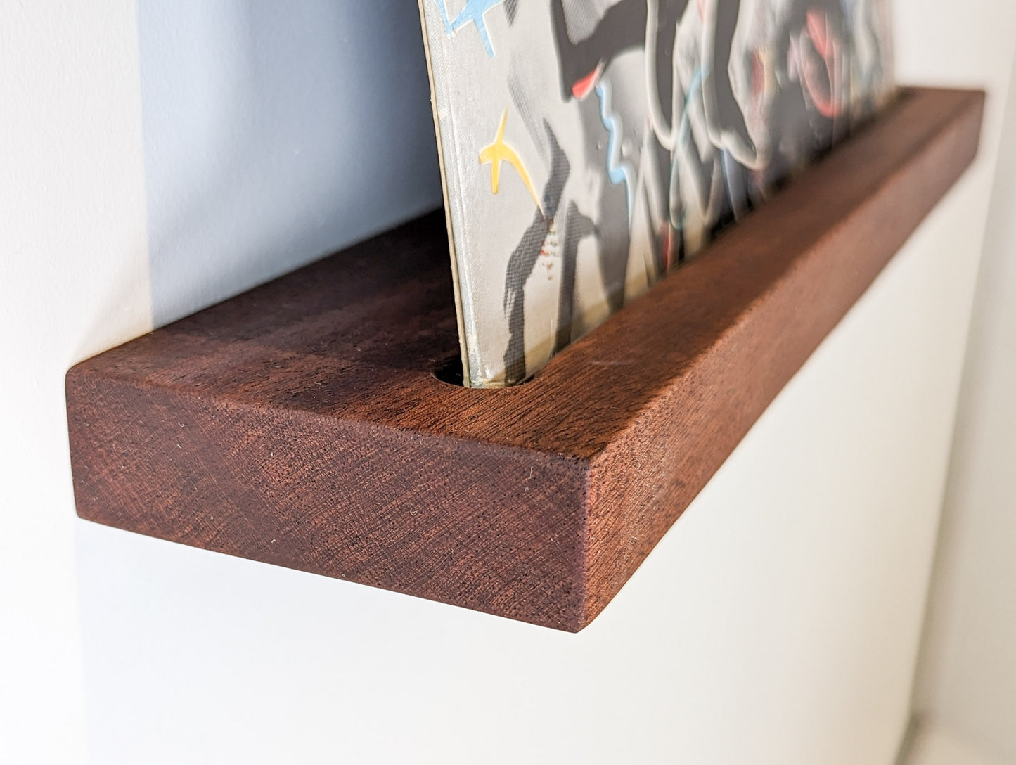 Side angled picture of a mahogany shelf with an album sleeve as decor.