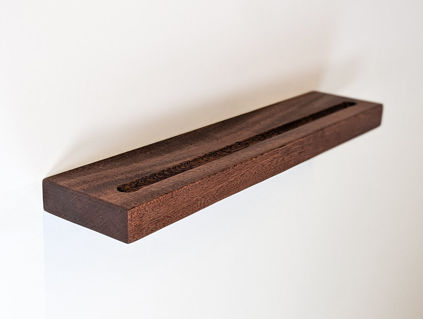A mahogany floating shelf with a groove is attached to a wall
