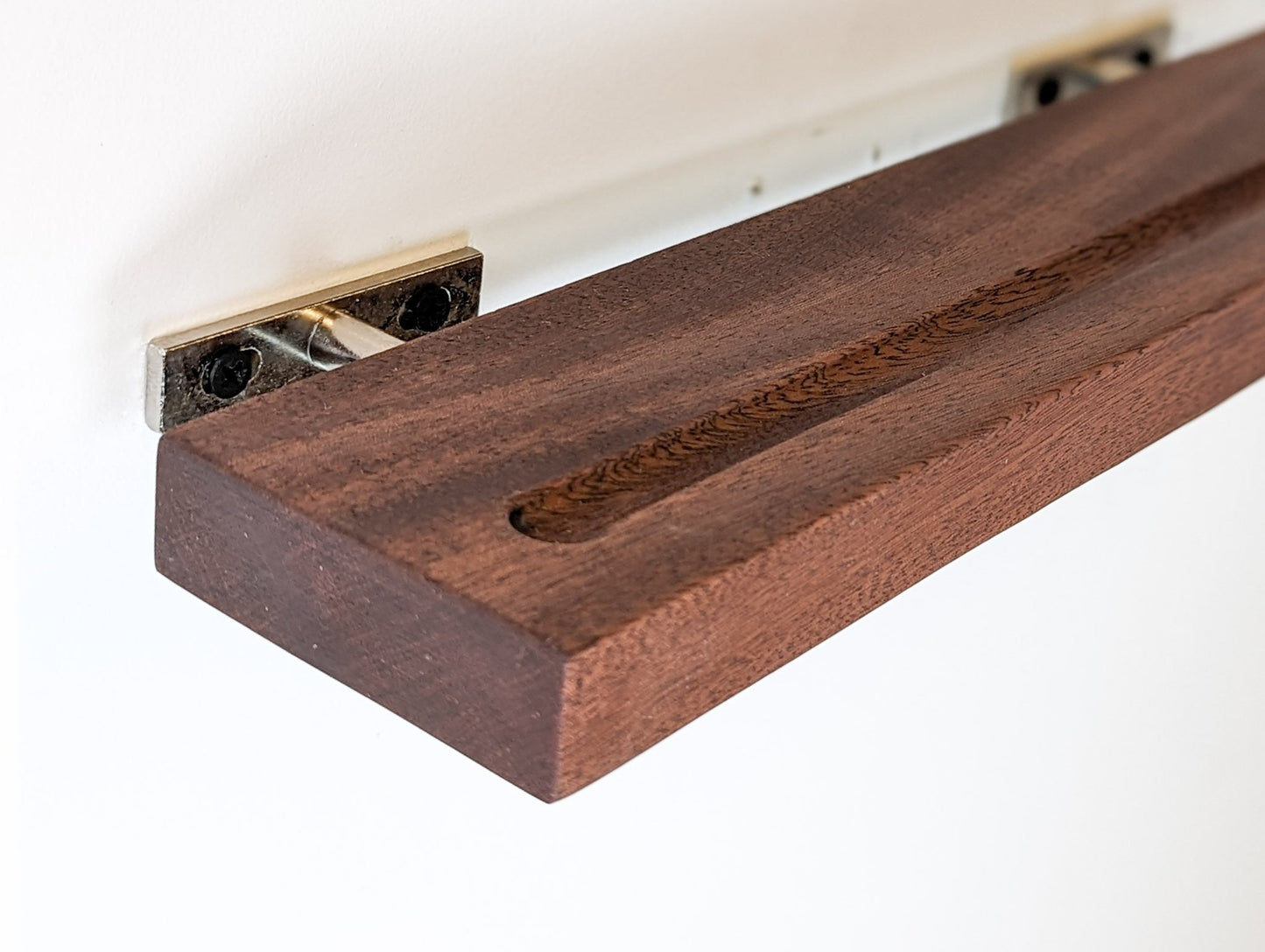 A mahogany shelf for vinyl records is sliding onto the hidden metal brackets that are attached to the wall.