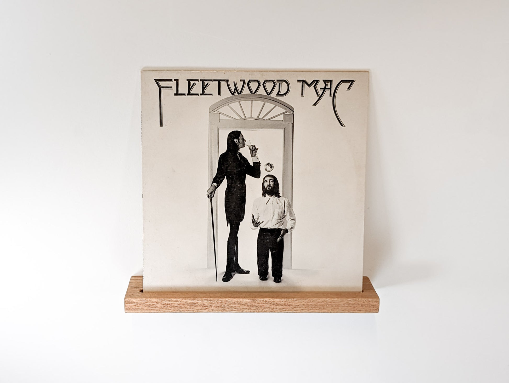 An oak floating shelf with a groove for vinyl records is attached to a wall.