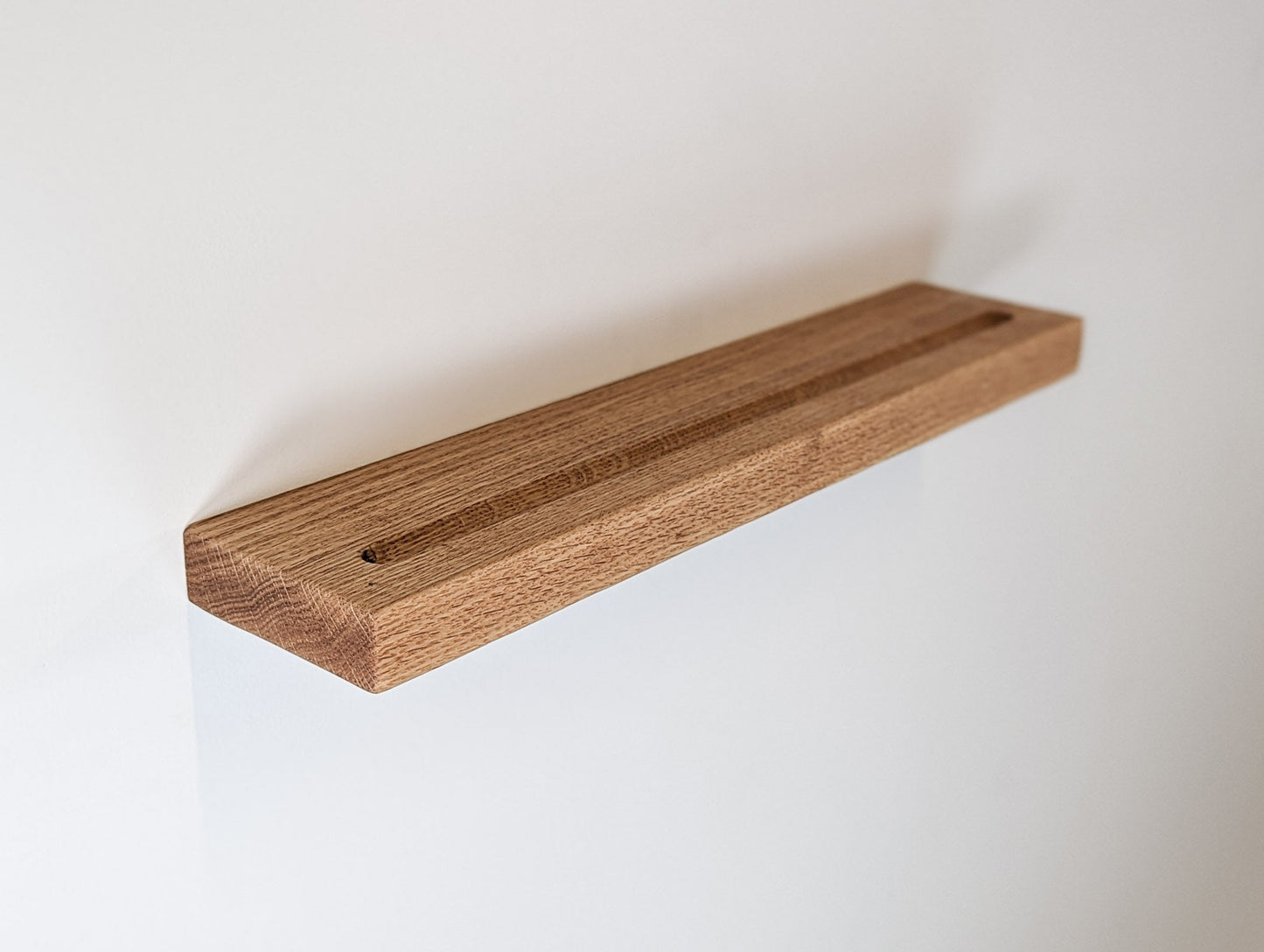 An oak floating shelf with rounded edges and a groove is attached to drywall.