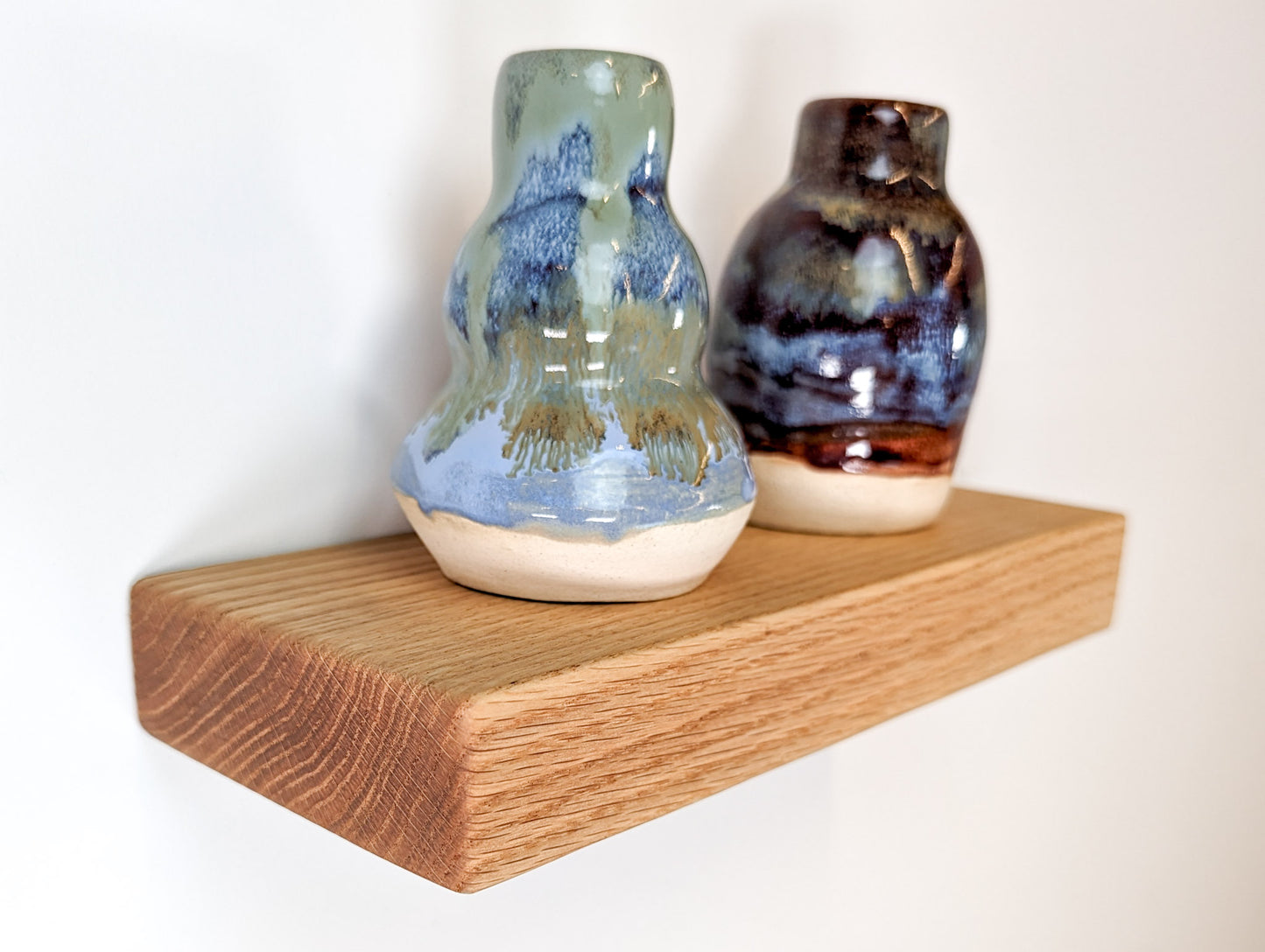 Two vases sit on top of a small thick oak shelf.