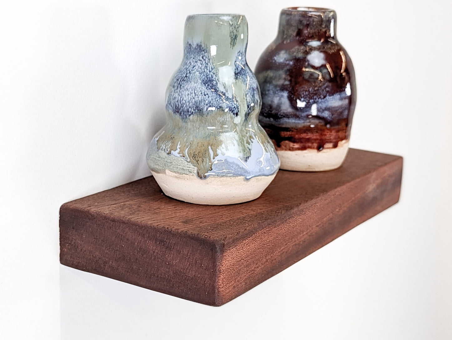 A blue vase and red vase rest atop a 4" x 10" mahogany shelf.