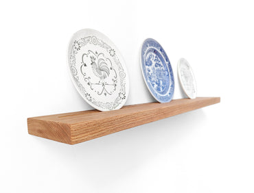 Three kitchen plates are displayed on a ledge shelf with a groove to securely hold them.