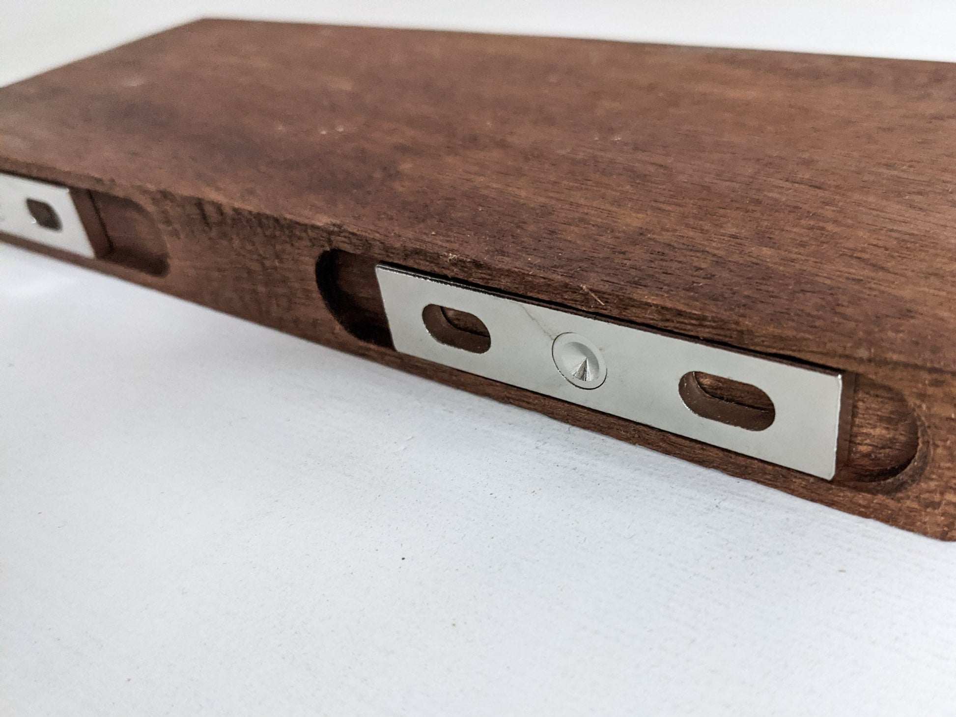 The back of a medium floating shelf in mahogany demonstrating how two silver brackets securely stabilize the floating shelf to the wall.