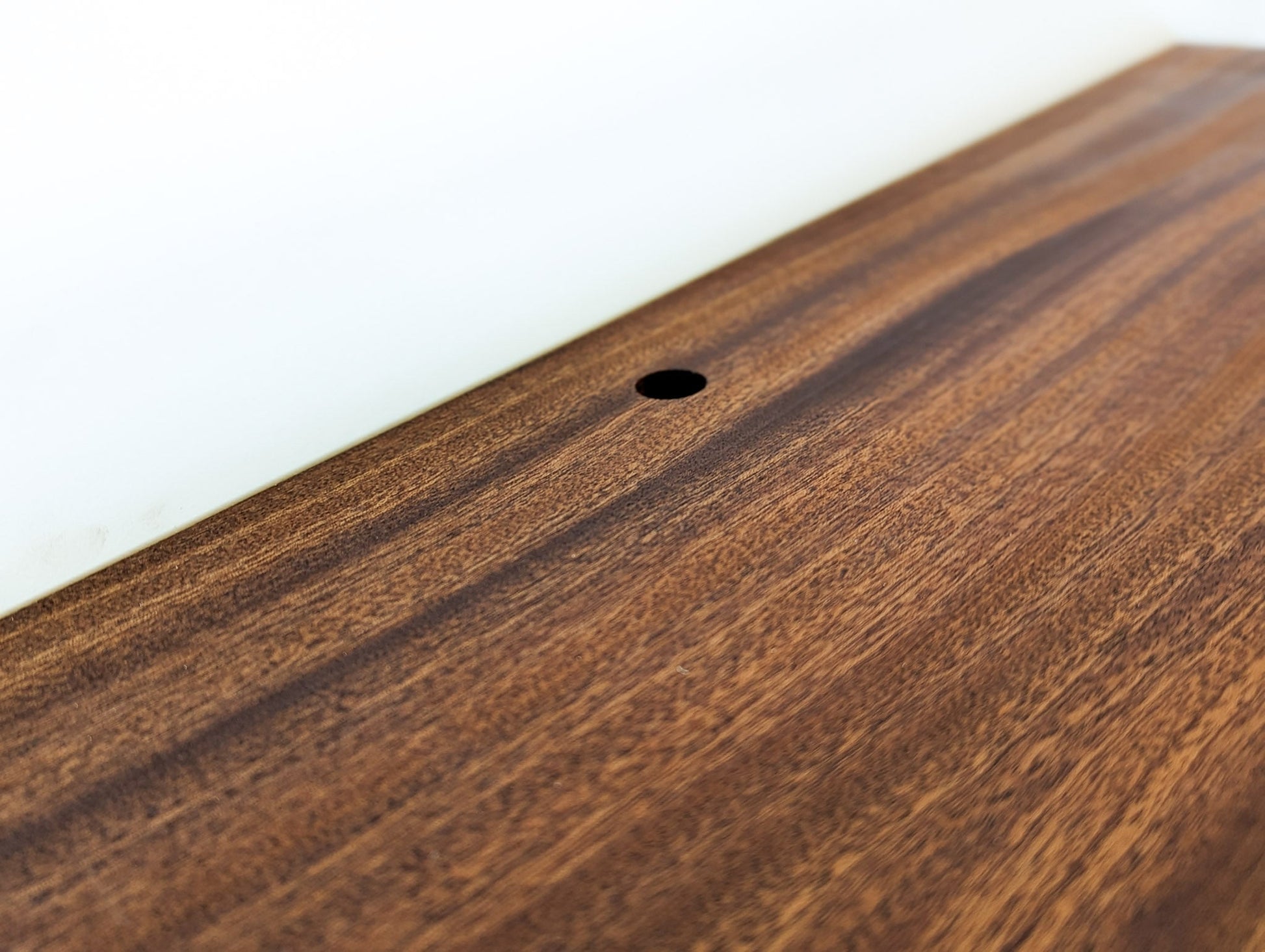 Zoomed in picture of a cord hole in a mahogany floating shelf attached to drywall.