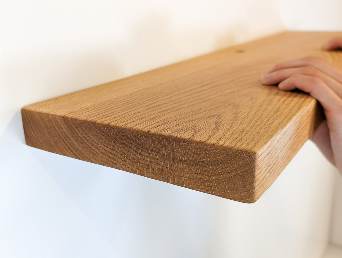 Close up picture of a hand pushing an oak shelf with a grommet hole onto a wall.