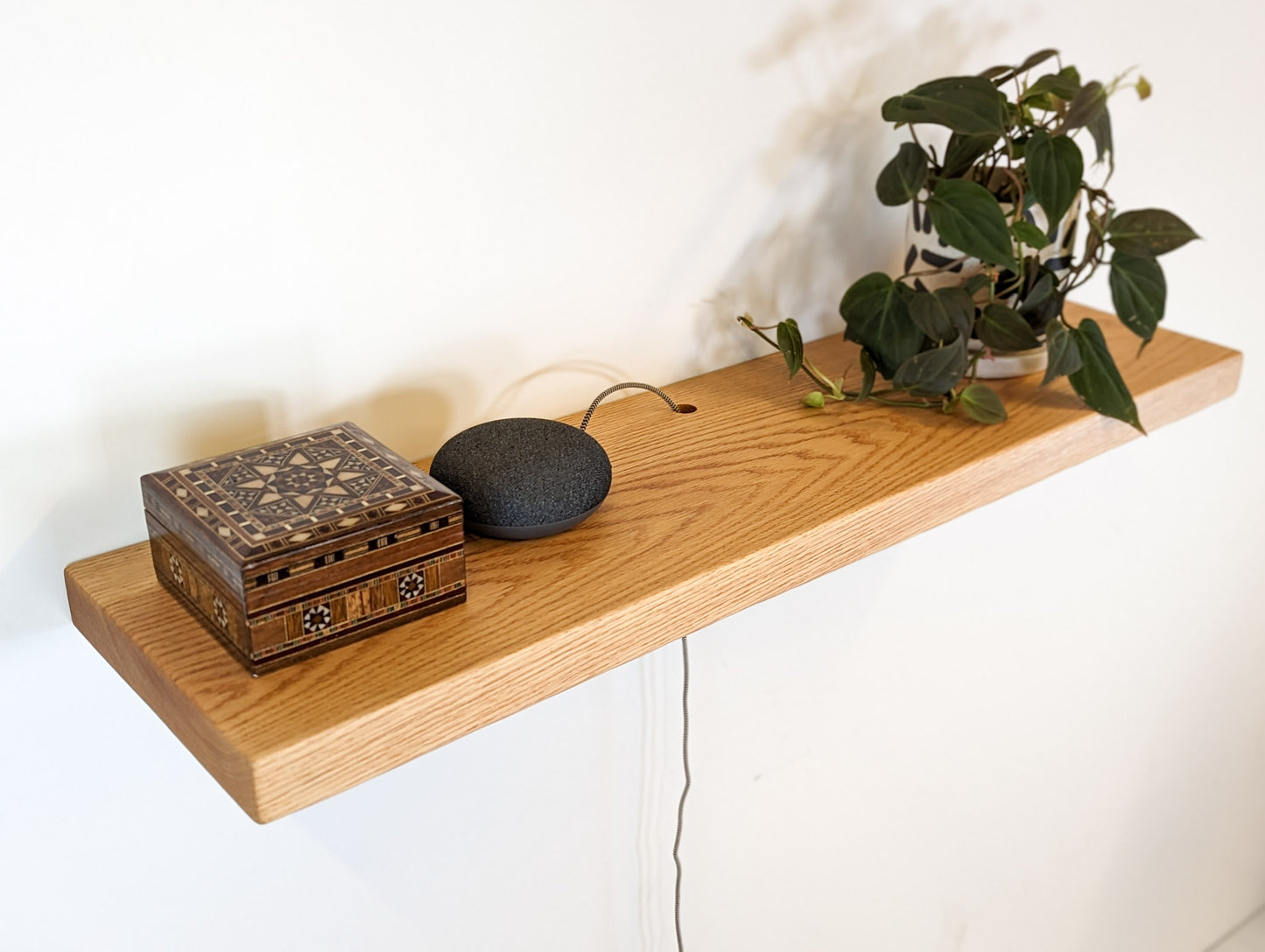 An oak shelf with a cord hole displays a box, speaker, and plant.