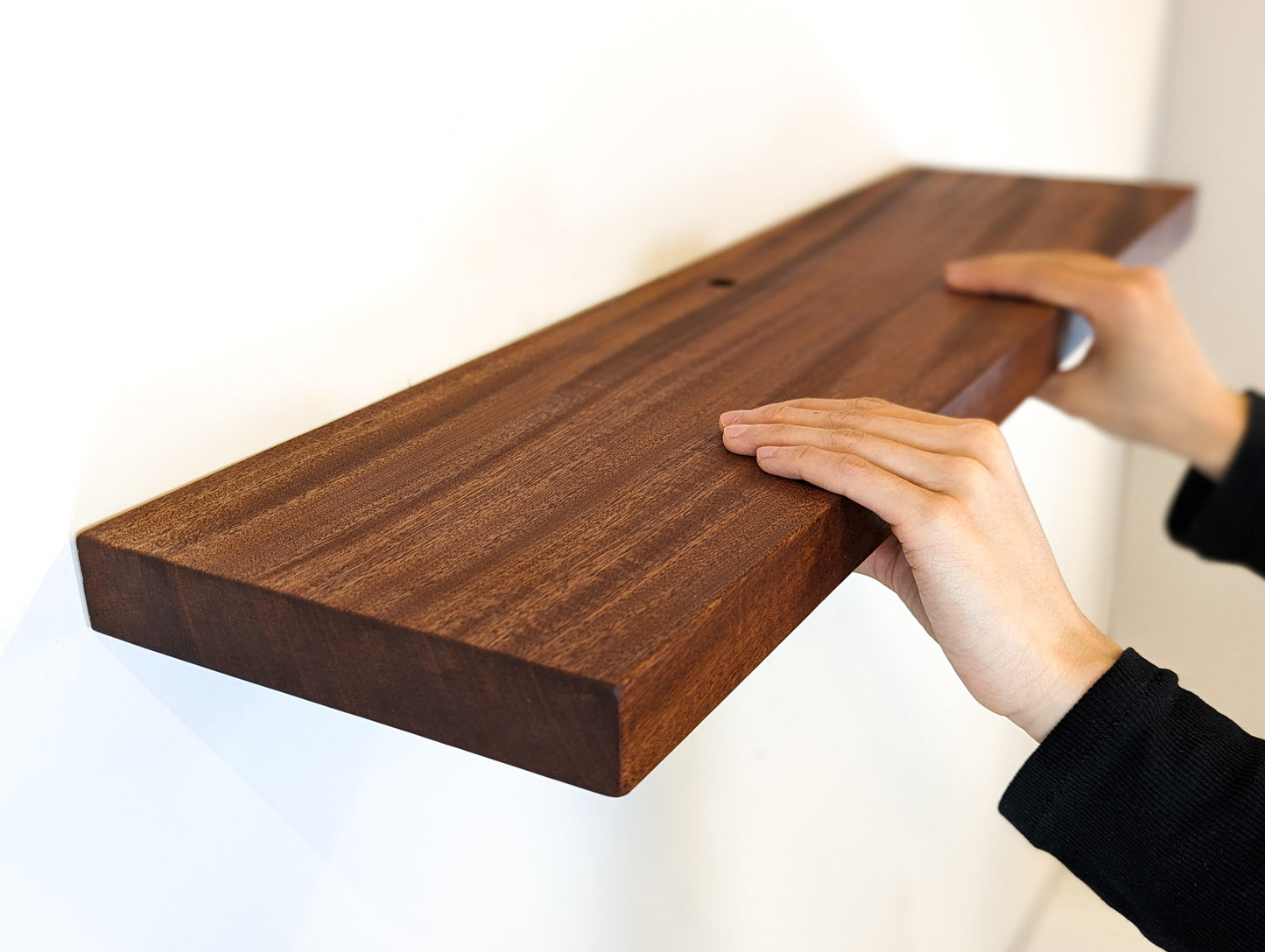 Two hands hold onto a mahogany shelf with a cord hole.