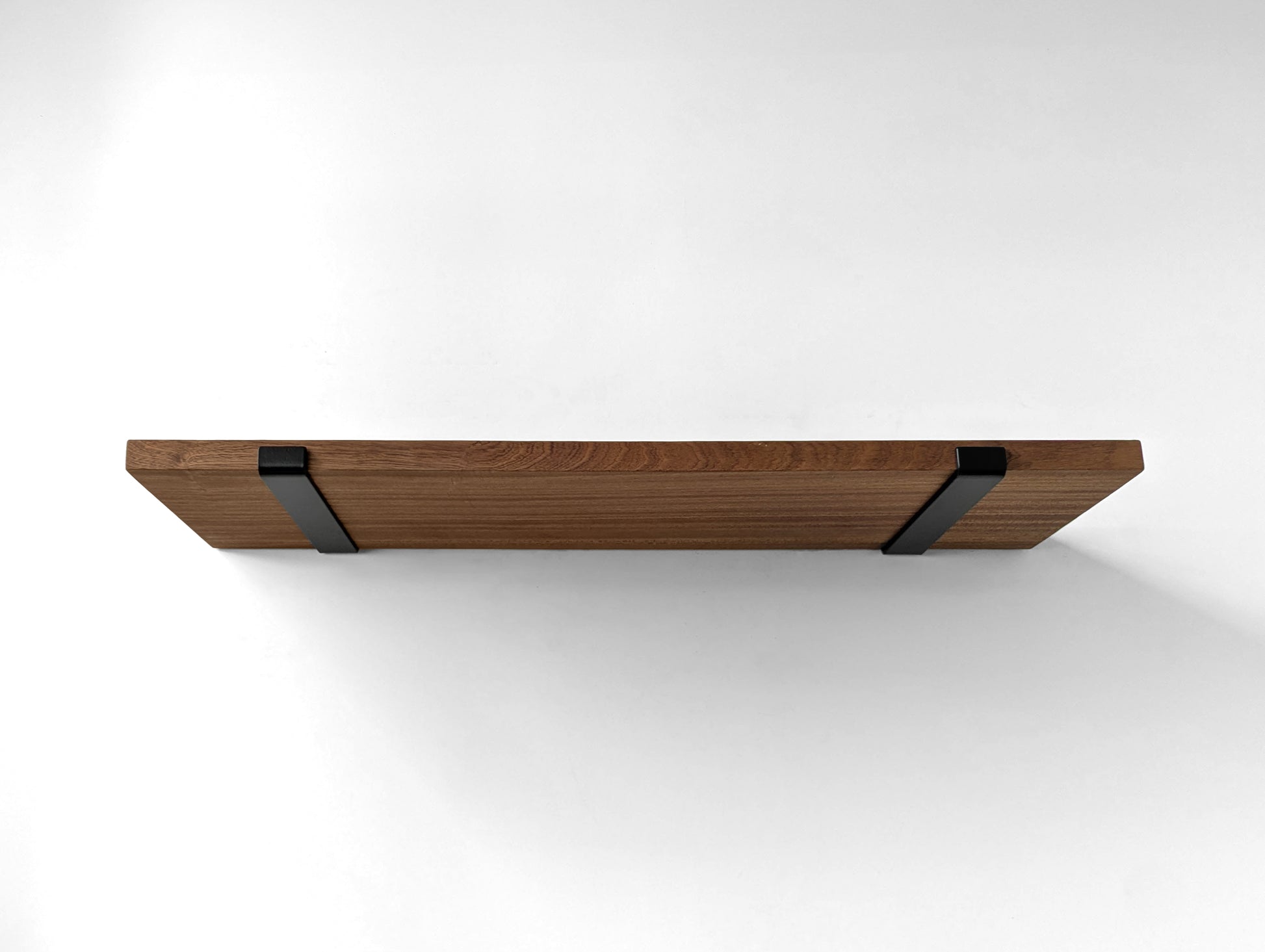 Underside of a large thick mahogany shelf and two black brackets wrapping around the front side to hold from slipping.