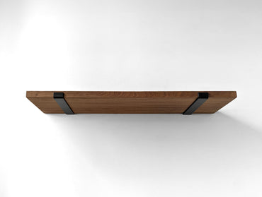Underside of a large thick mahogany shelf and two black brackets wrapping around the front side to hold from slipping.