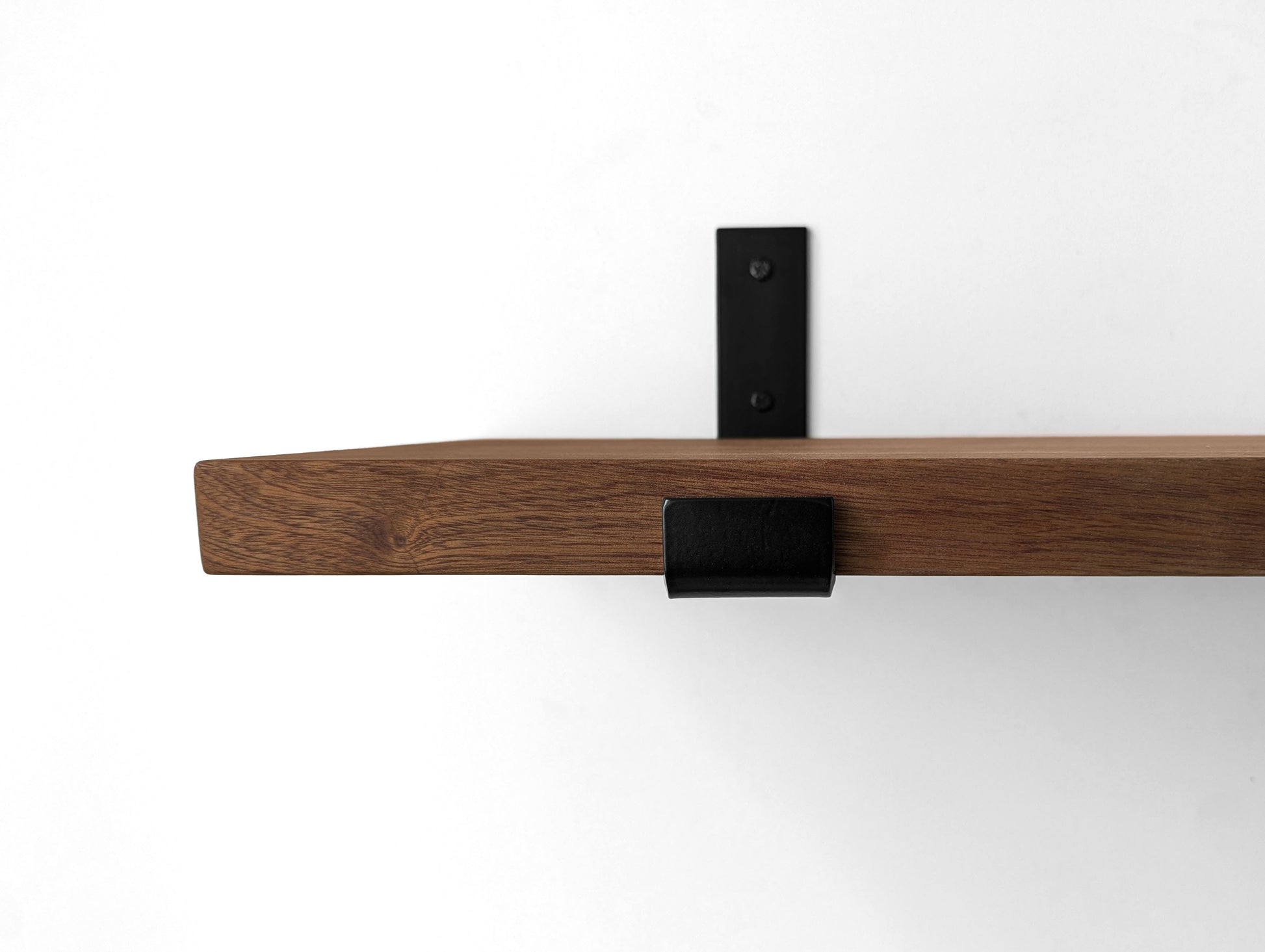 Close up photo of a black metal j bracket and a beautiful mahogany shelf.