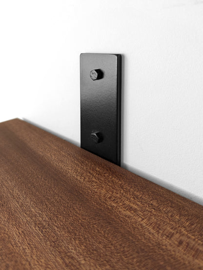 Close up photo of a black powder coated bracket attached a white wall with toggle bolts.