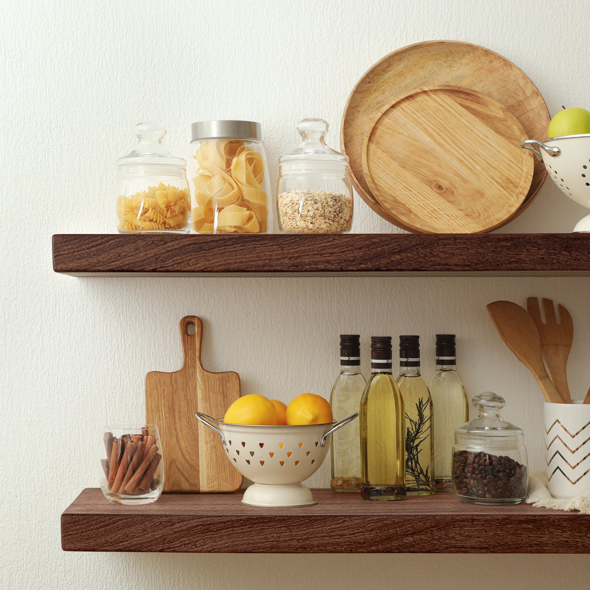 Two thick mahogany shelves on a wall in a kitchen with kitchen items displayed on the shelves.