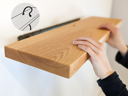 Two hands push a thick oak shelf with a grommet hole onto a metal bracket. Text is shown overlaying the image that says "Cord Hole" with an arrow to the grommet hole on the shelf.