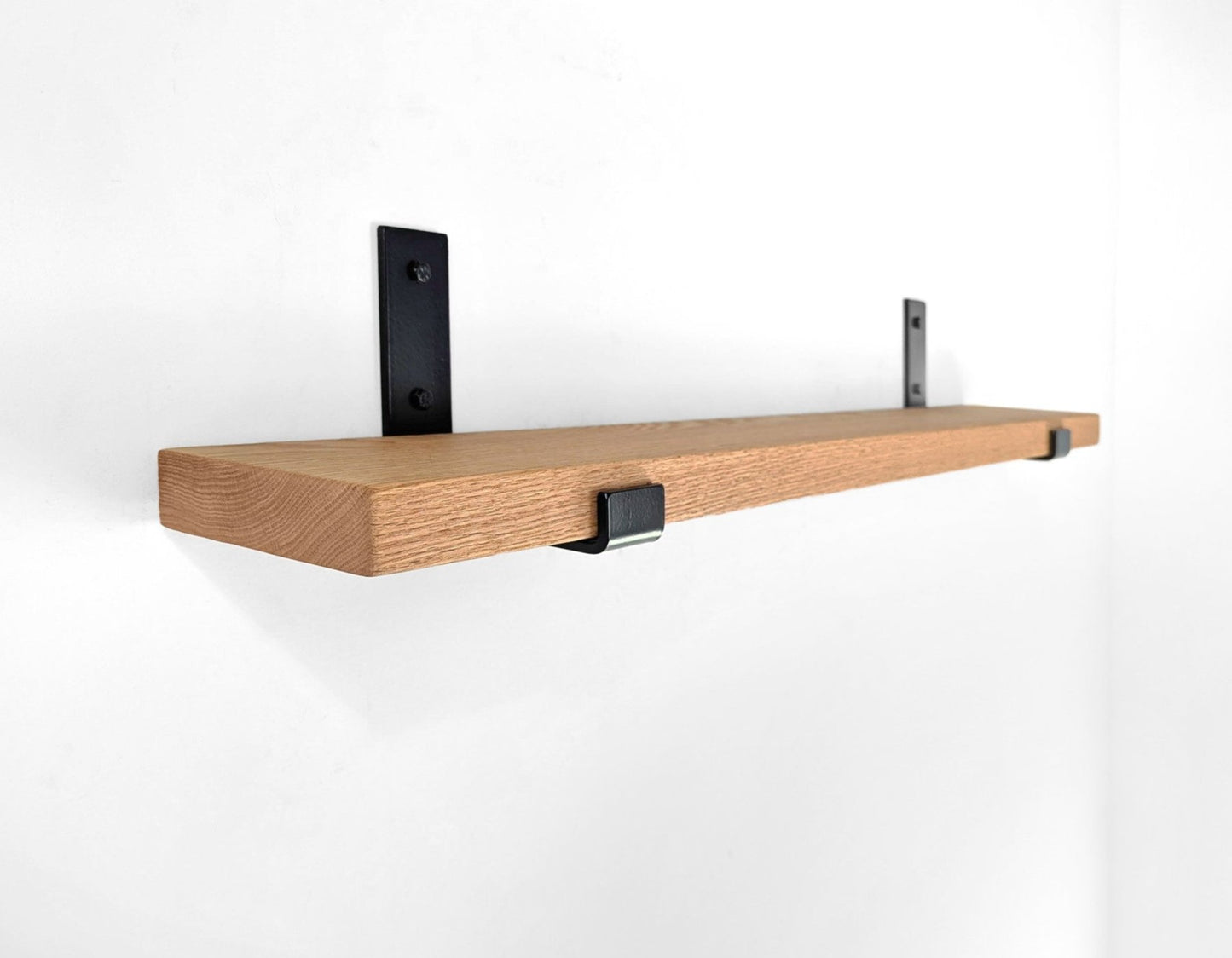 A thick oak shelf with two powder coated steel brackets hangs on a white wall.