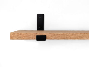 Zoomed in front view of an oak shelf with a black powder coated J bracket installed on the wall.