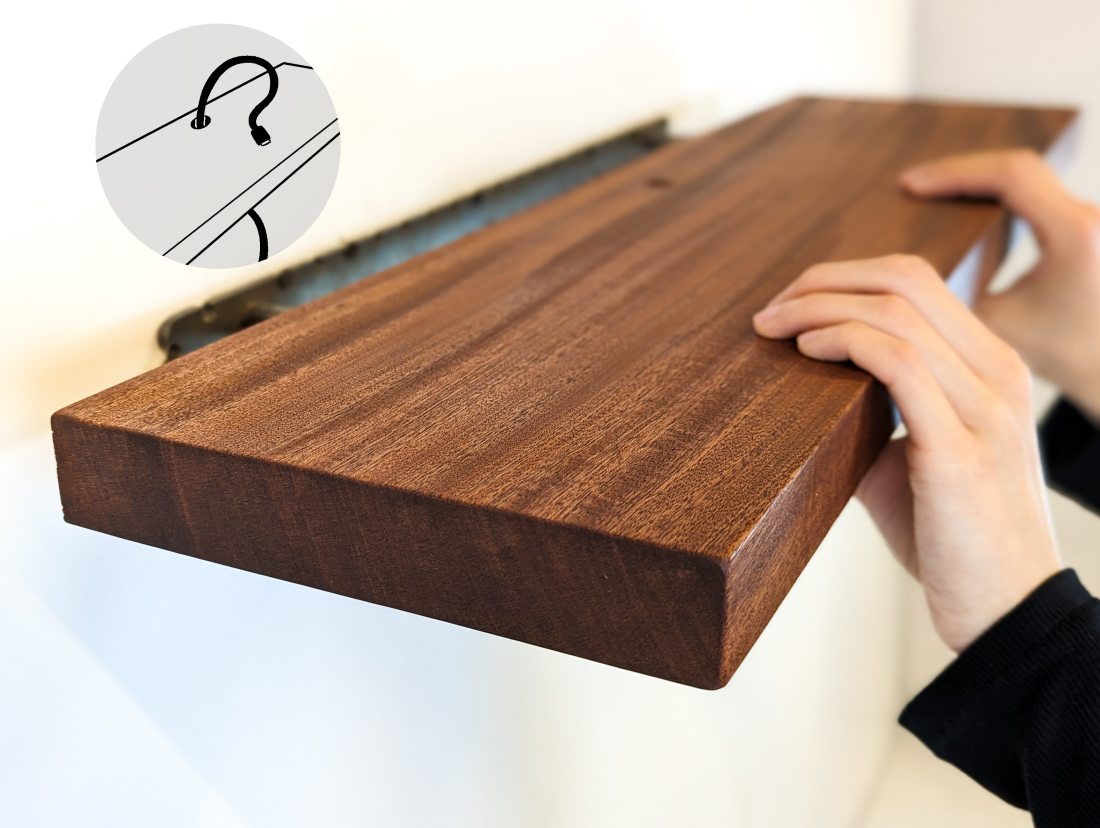 Two hands push a thick mahogany shelf with a grommet hole onto a metal bracket. Text saying "Cord Hole" points to the grommet hole in the middle of the shelf.