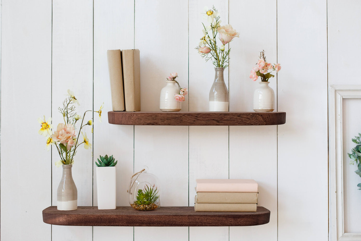 Thin mahogany wooden shelves with books, vases, and plants against a white wall.