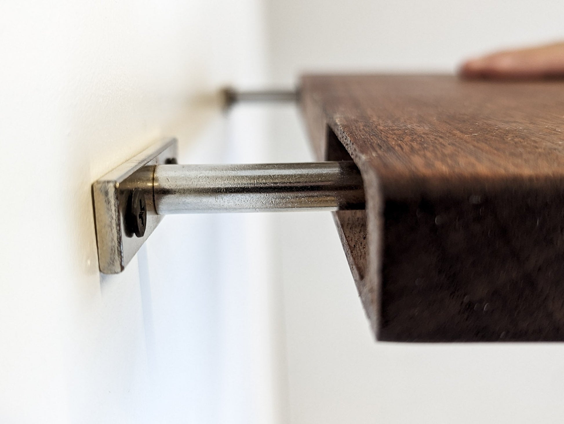 Side view of a mahogany floating shelf fitting into two metal brackets attached to the wall