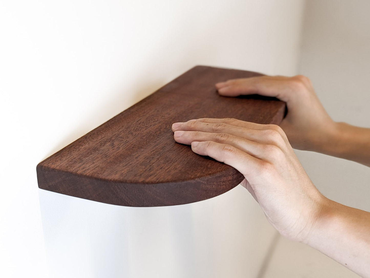 Two hands rest on a mahogany floating shelf with curved corners