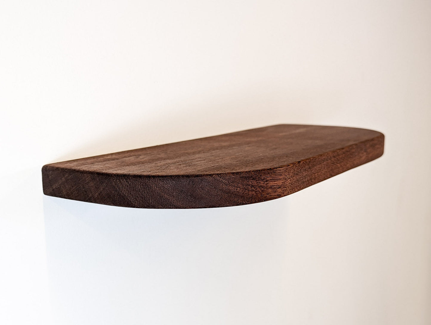 angled view of a mahogany floating shelf with soft curved corners