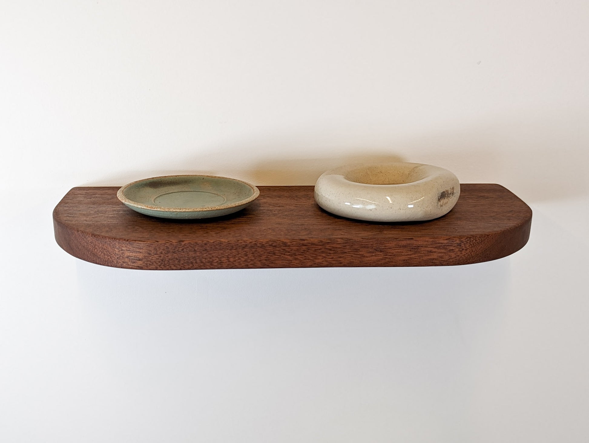 Front view of a rounded corner mahogany floating shelf with two decor items on top