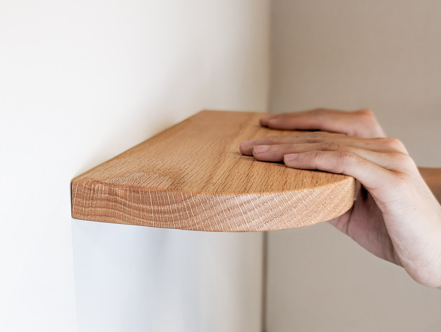 Two hands rest on an oak shelf with rounded corners against the wall