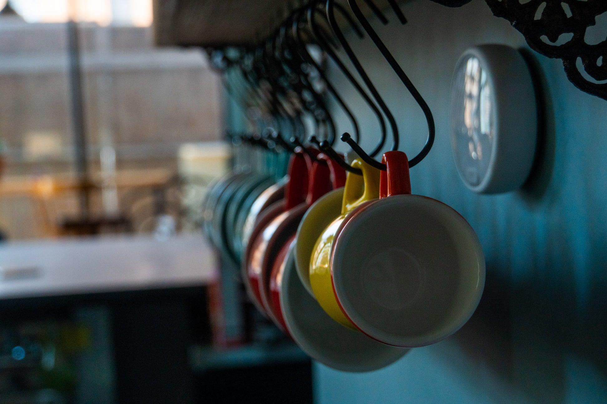 A focused shot of the hanging various coffee and tea mugs. They are hanging from S hooks which are hanging from the underside of the shelf.