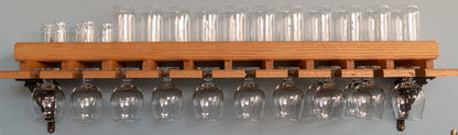 A front view of our Oak or Mahogany Beer Glass Shelf. A raised lip secures eleven tall beer glasses and 5 short beer glasses on top while 12 tulip beer glasses hang upside down below. The shelf is secured to the blue wall by cast-iron brackets.