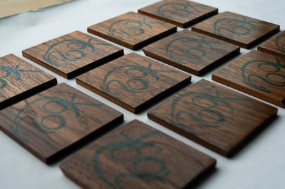 Three rows of four NookWoodworking coasters. These solid wood coasters are square with the word, "nook" stamped on them in large, rounded, blue, letters.