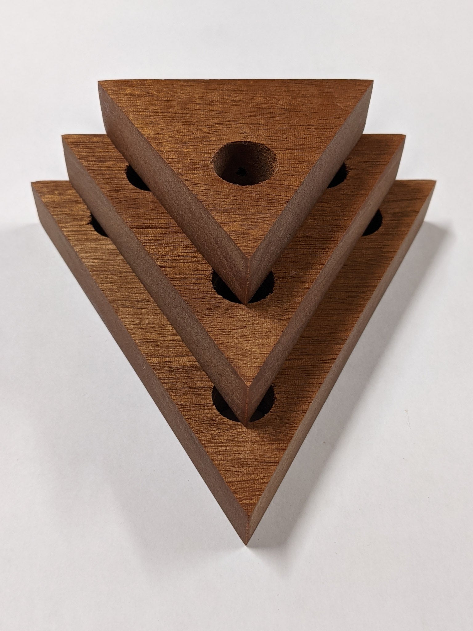 A set of three triangle mahogany propagation shelves sit one on top of the other with the largest at the bottom and the smallest on top. 