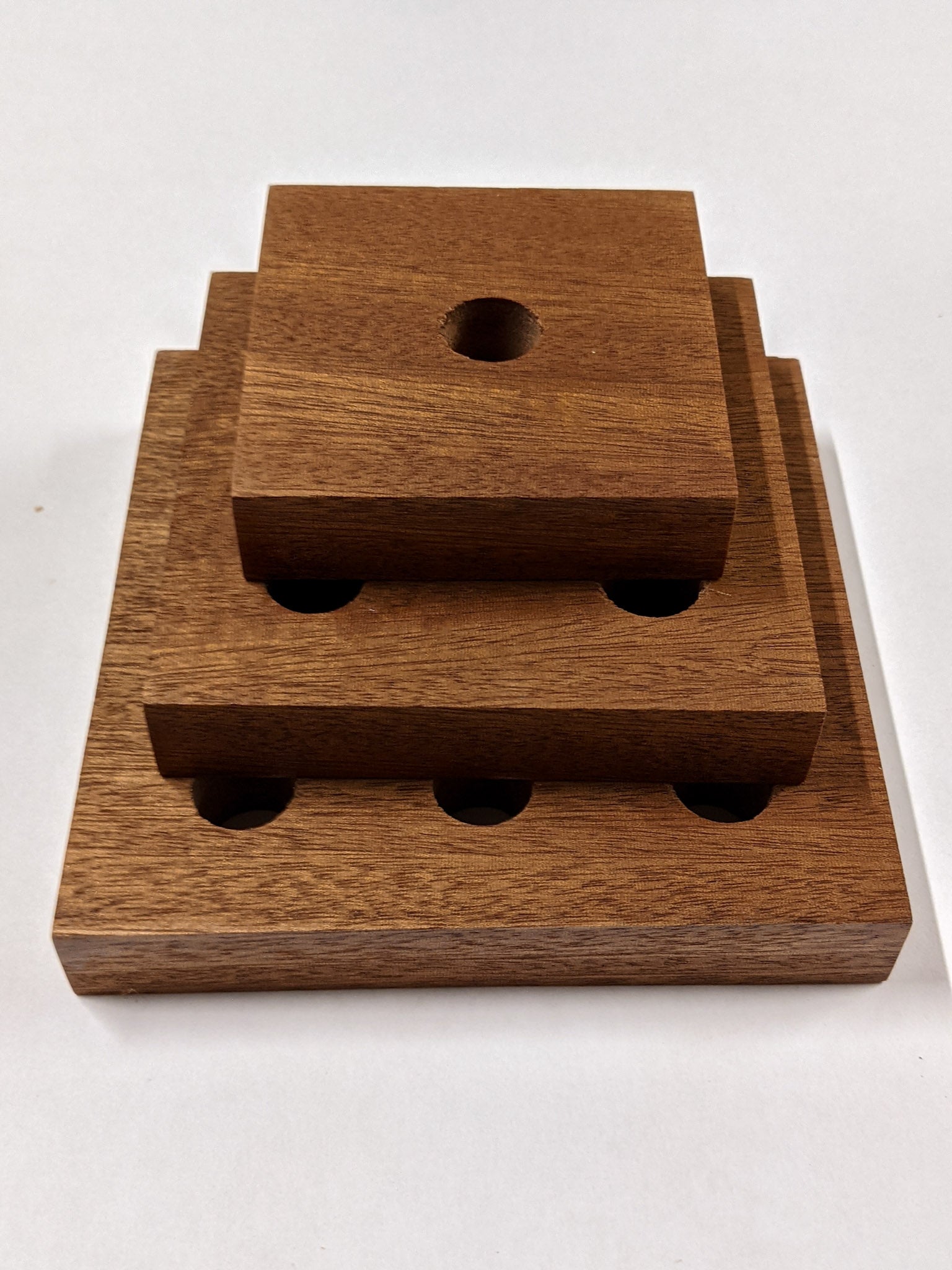 A set of three square mahogany propagation shelves sit one on top of the other with the largest at the bottom and the smallest on top.