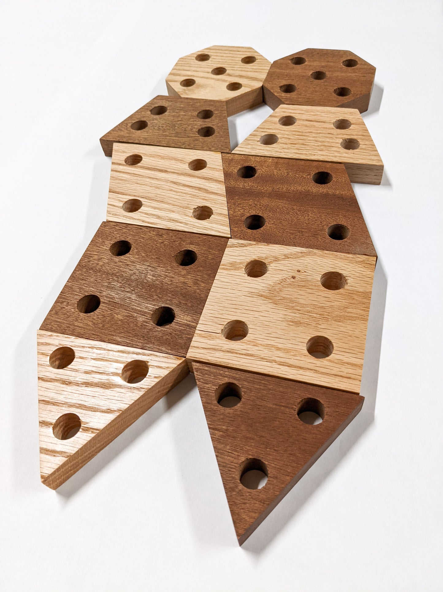 Each of the geometric propagation shelves is represented in oak and mahogany with four holes. From top to bottom, octagon, rhombus, trapezoid, square, and triangle. The triangle has three holes. 