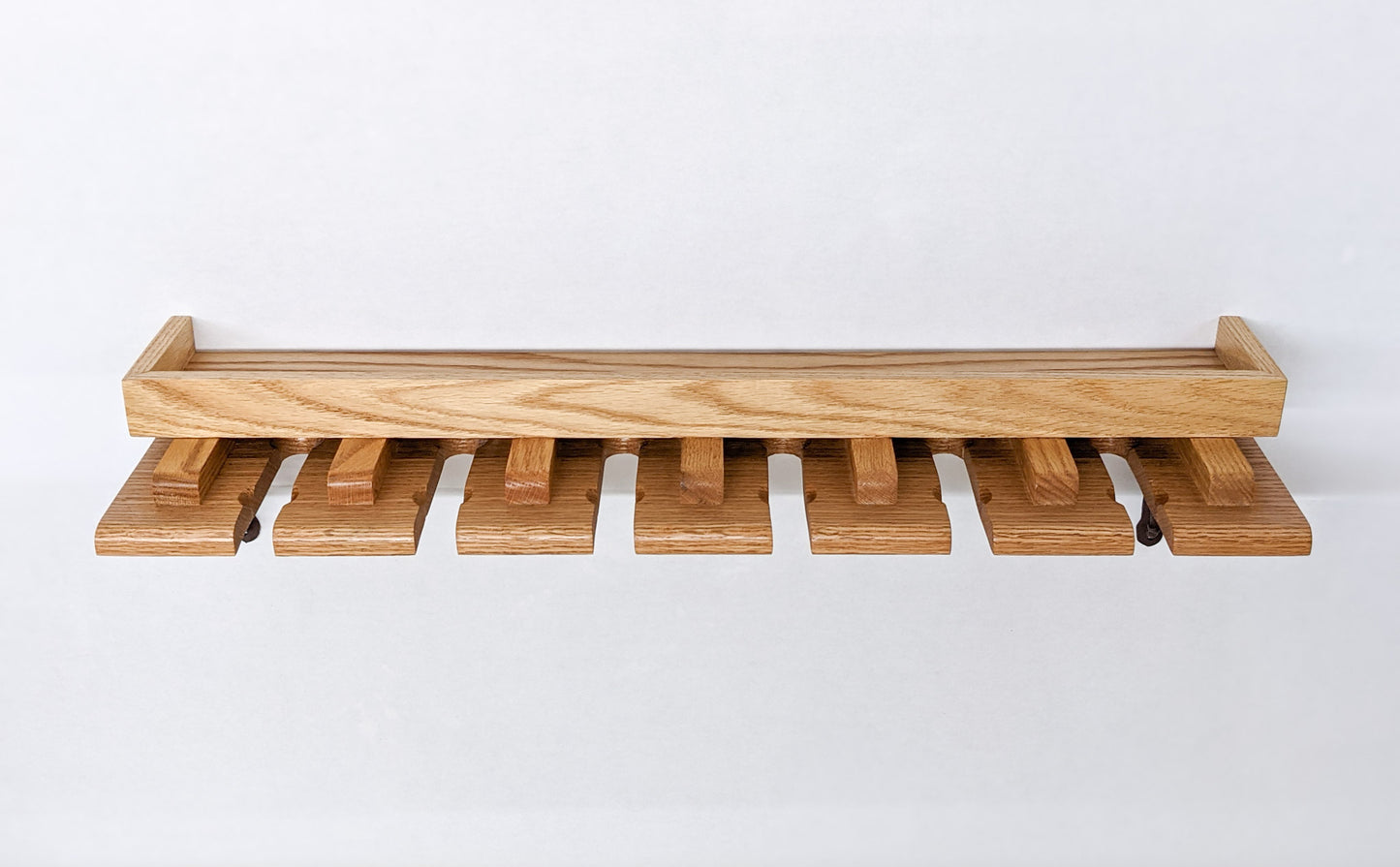 A head-on view of an empty Oak Beer Glass Shelf. The attractive edge on top is raised for secure glass storage and the depth of the shelf if highlighted to demonstrate the ability to easily hang up to two tulip beer glasses per slat. There are seven slats and 6 notches to slide the tulip glasses in. 