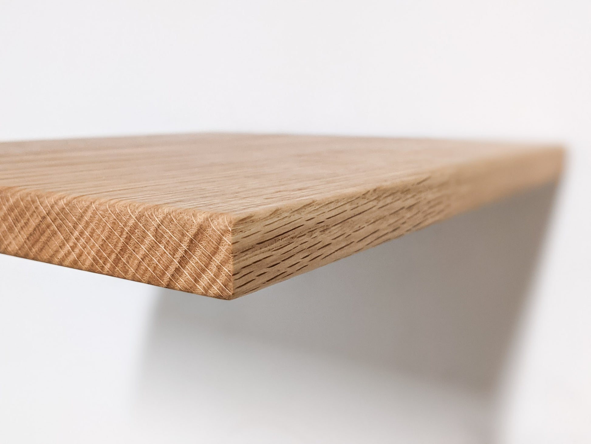 A close-up of the soft rounded corners and natural grain of a medium oak wood shelf. 