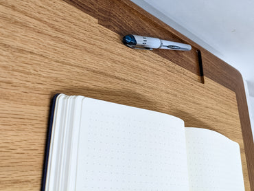 A close-up of the top portion of our leather cushion writing lap desk. The oak interior gracefully meets the mahogany border and a pen rests in a rectangular pen divet. A bullet journal is open and showcasing two blank pages.