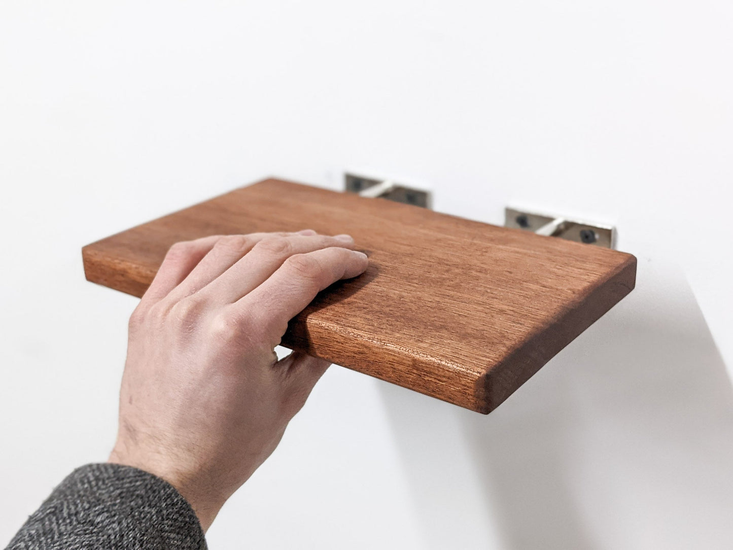 A hand sliding the medium mahogany floating shelf onto two silver brackets.
