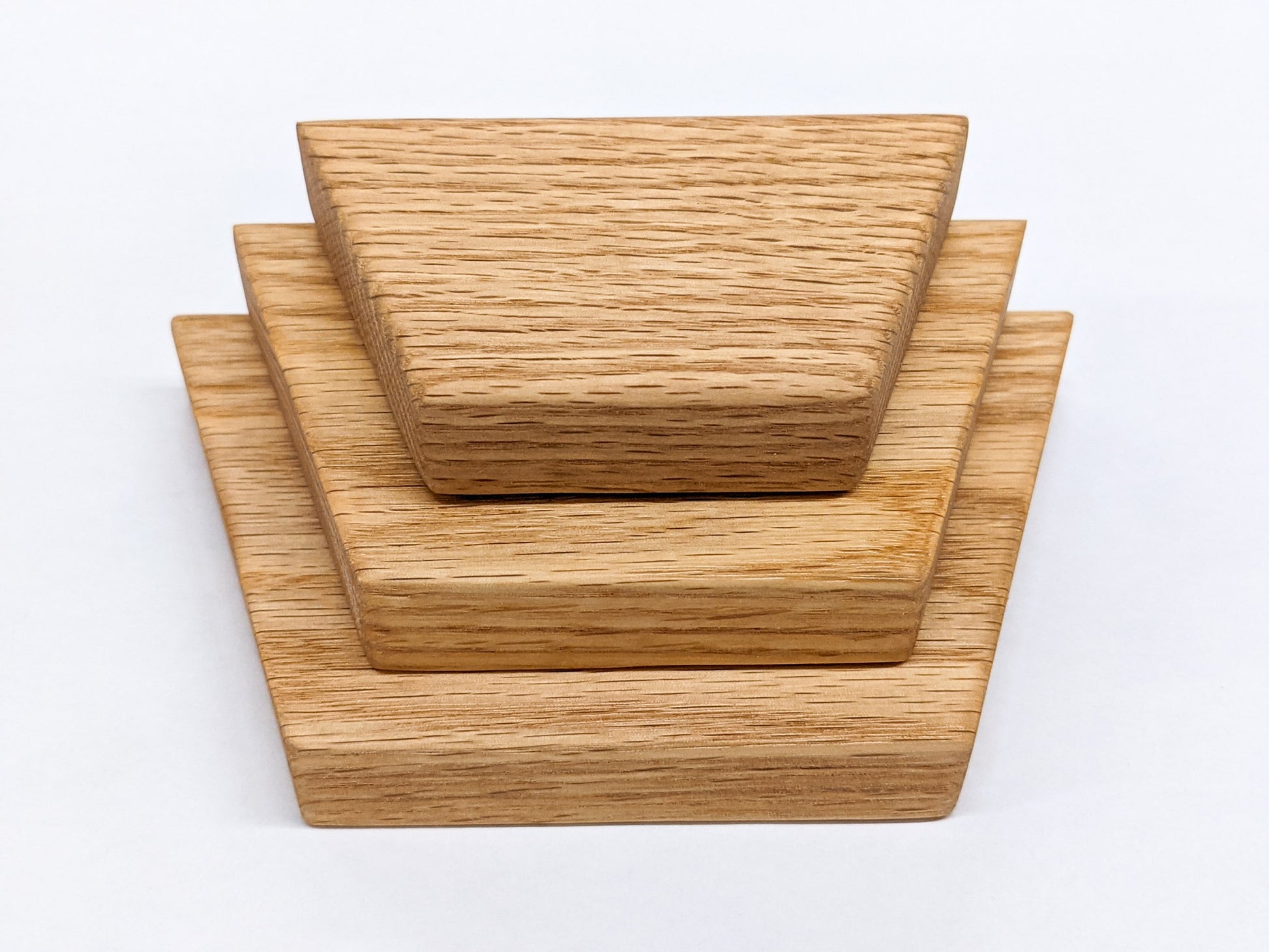 Three trapezoid floating shelves in oak sit on top of the other in varying sizes from largest to smallest.