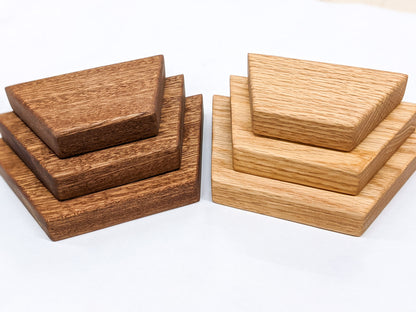 Three trapezoid floating shelves in oak sit on top of the other in varying sizes from largest to smallest. Across from them, three mahogany trapezoid floating shelves sit on top of another from largest to smallest sizes.