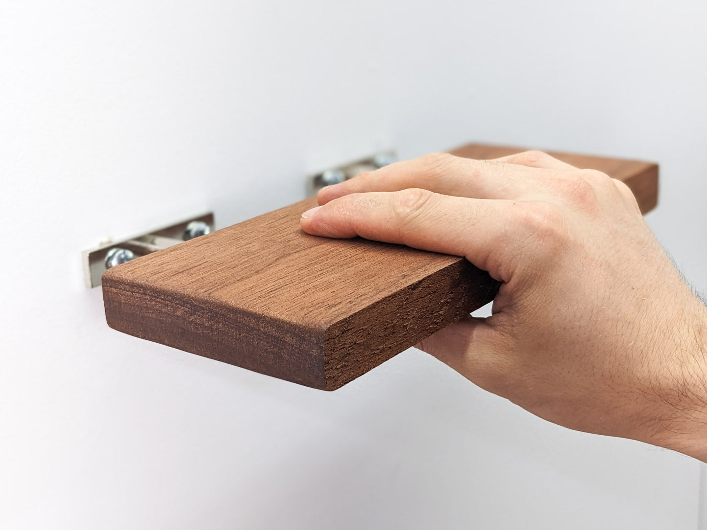 Our medium mahogany live edge floating shelf is in the process of being installed. A hand grips the front top and bottom, lowering it onto the screw for easy-to-install wall mounting.